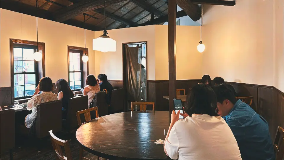 Zweite Etage mit sichtbaren Holzbalken, schräger Decke, Fenstersofas und einem großen runden Tisch